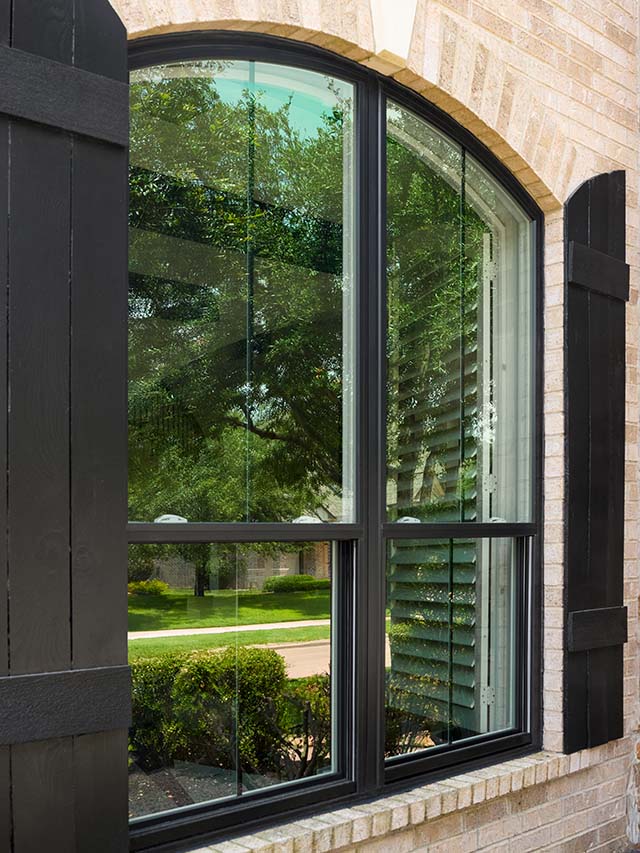 Arched window with black shutters on brick home exterior.