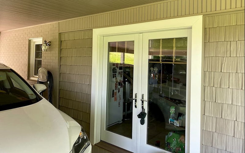 A white car is parked next to a home with a two-panel hinged patio door