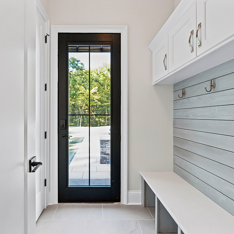 Mudroom with black-framed glass door, built-in bench, hooks, and white storage cabinets.