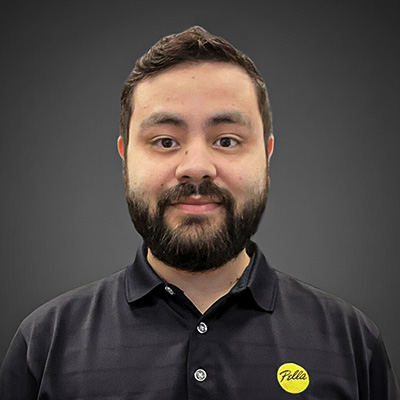 a headshot of a man with dark hair and facial hair smiling at the camera while in front of a gray background.