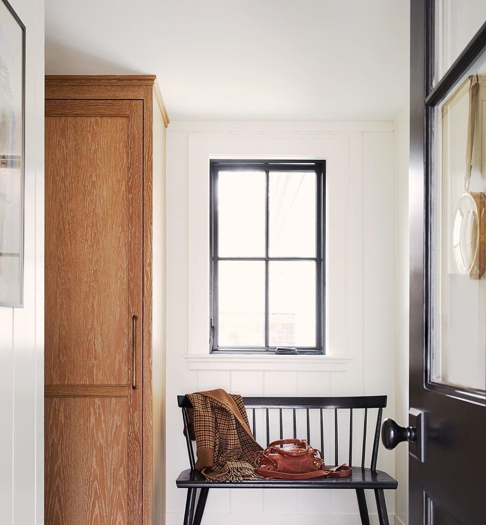 A black casement window above a bench in an entryway.