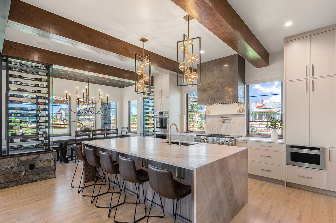 Contemporary kitchen featuring a large marble island, leather bar stools, wine storage wall, pendant lighting, and exposed wooden ceiling beams.