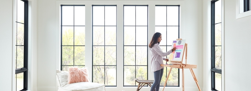 young woman painting surrounded by several pella black-trimmed windows