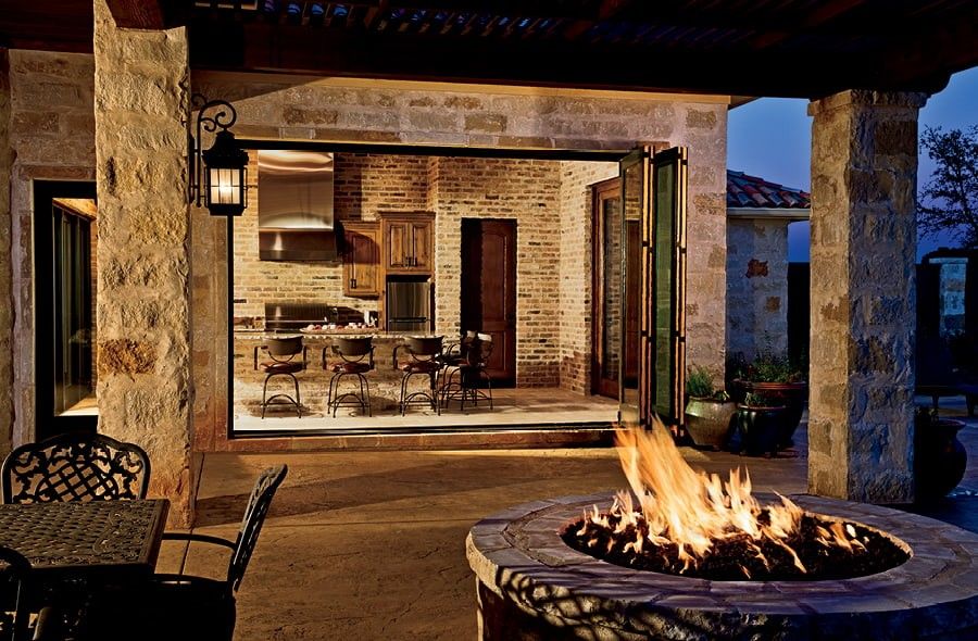 Exterior view of outdoor space with a firepit that looks through a Folding Glass Door into European style kitchen