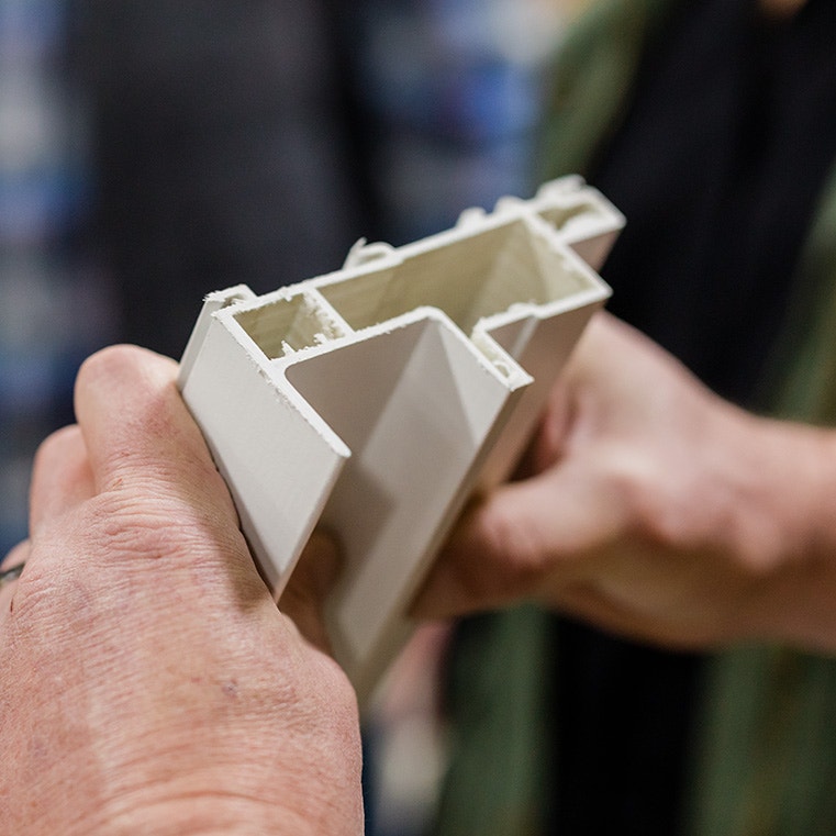 A close-up of a person holding a cross-section of an interior vinyl window frame, showcasing its design.