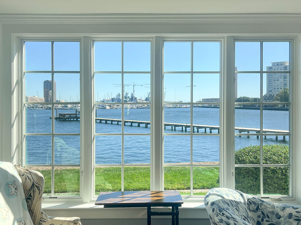 Interior view through Lifestyle double hung white windows showcasing a bright waterfront scene with a pier and boats under a clear blue sky.