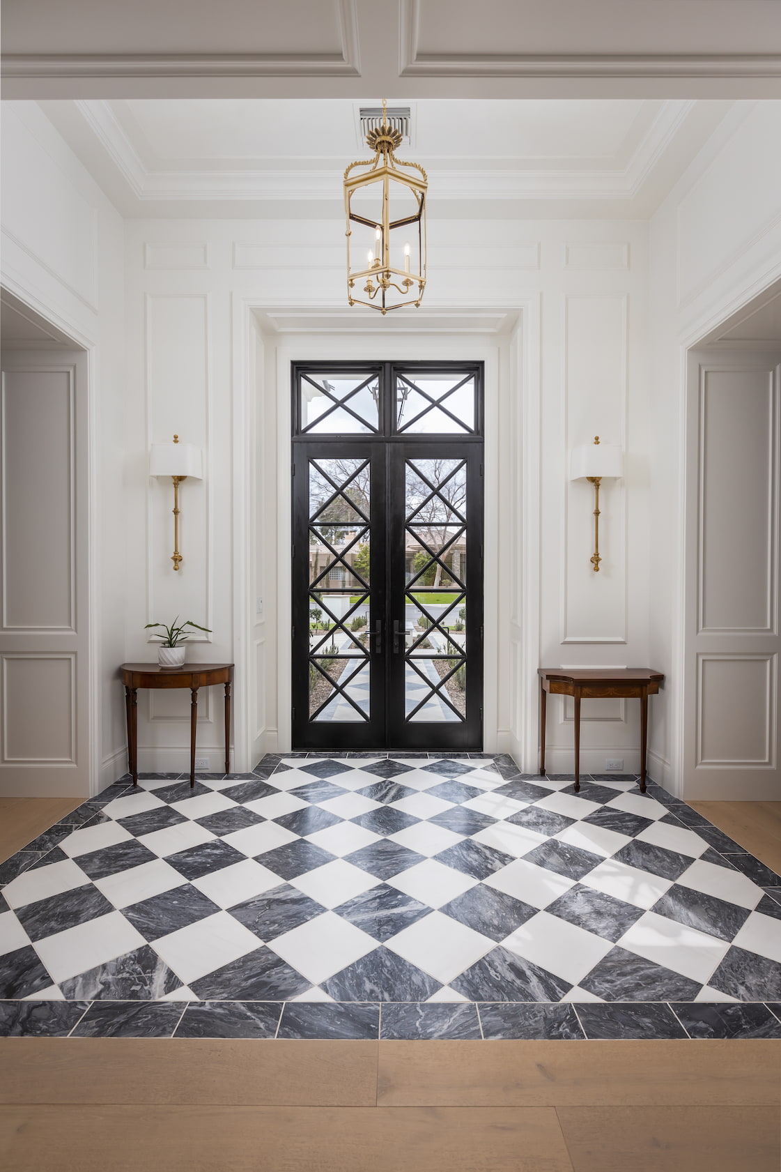 The foyer of an Arizona home features custom black double doors, gold light fixtures and tiled floors.