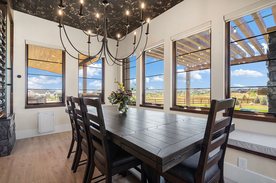 Contemporary dining room featuring a dark wood table, stylish chandelier, large windows with scenic outdoor views, and pergola-covered patio.