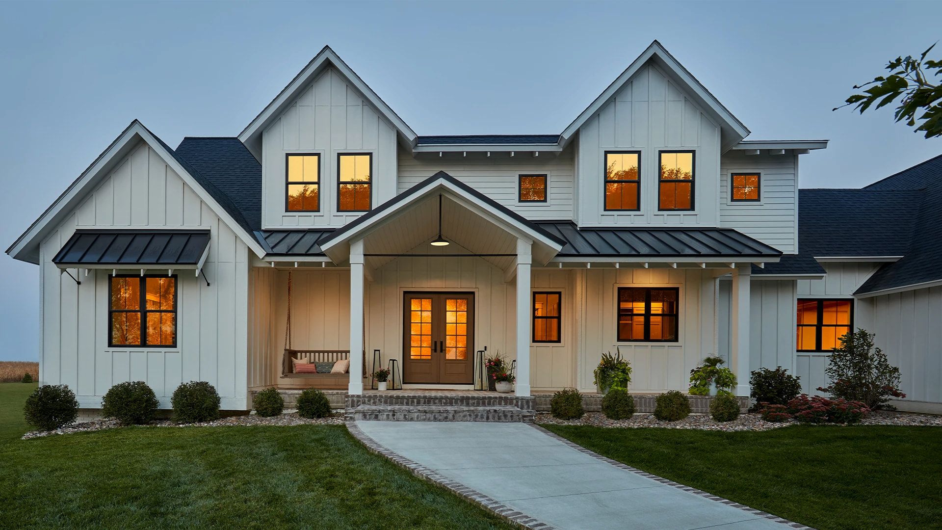 A large white farmhouse-style home that has the sunset reflected in the Pella windows and entry doors.