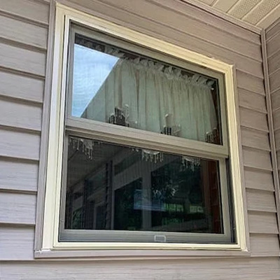 A large double-hung window with a white valance on the interior is outdated and ready for replacement.