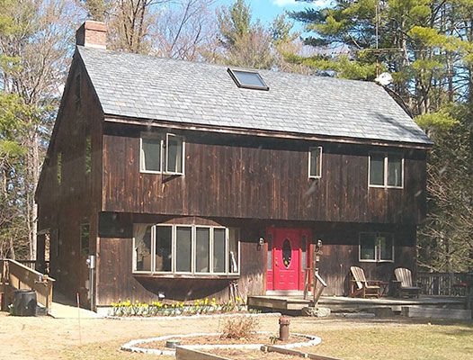 A wooden house exterior before renovation, featuring red windows and a red front door.
