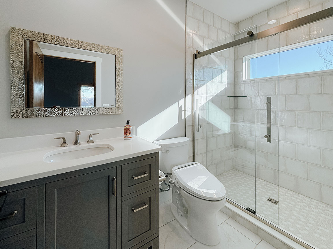 Modern white bathroom with frameless glass shower and gray vanity.