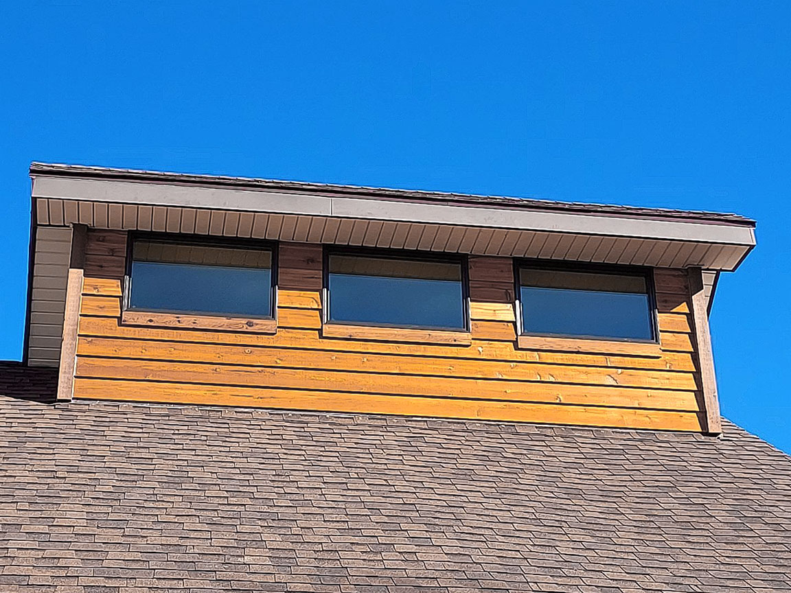 A wooden window set on a sloped roof against a clear blue sky, illustrating topeka window replacement.