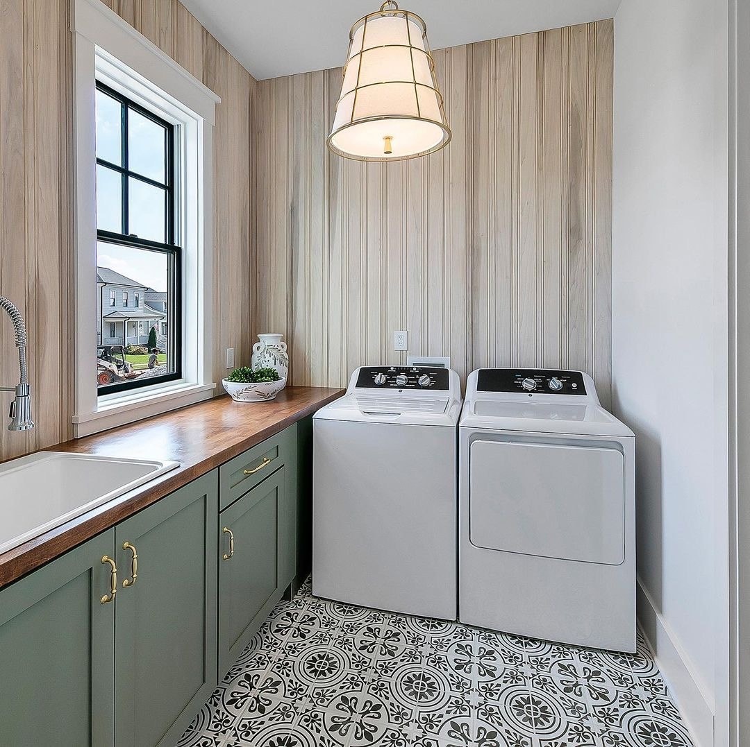 A black laundry room window is over light green cabinets, next to the washer and dryer.