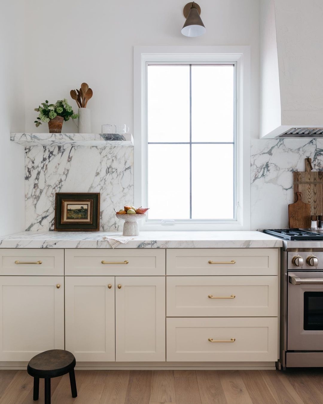 A light kitchen with a white casement window set between marble backsplash.