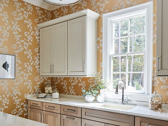 A traditional kitchen with yellow patterned wallpaper and a white window over the sink.