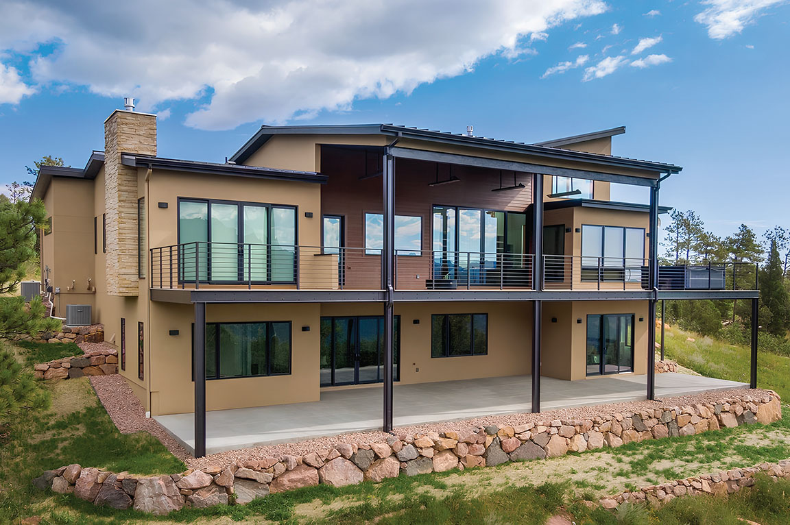 A tan house exterior showcasing black windows and patio doors, surrounded by greenery.