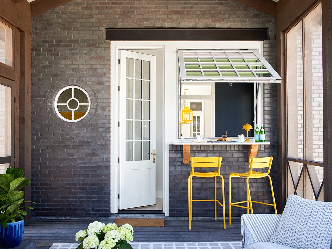 White patio door on a gray brick wall beside yellow barstools and a pass-through window.
