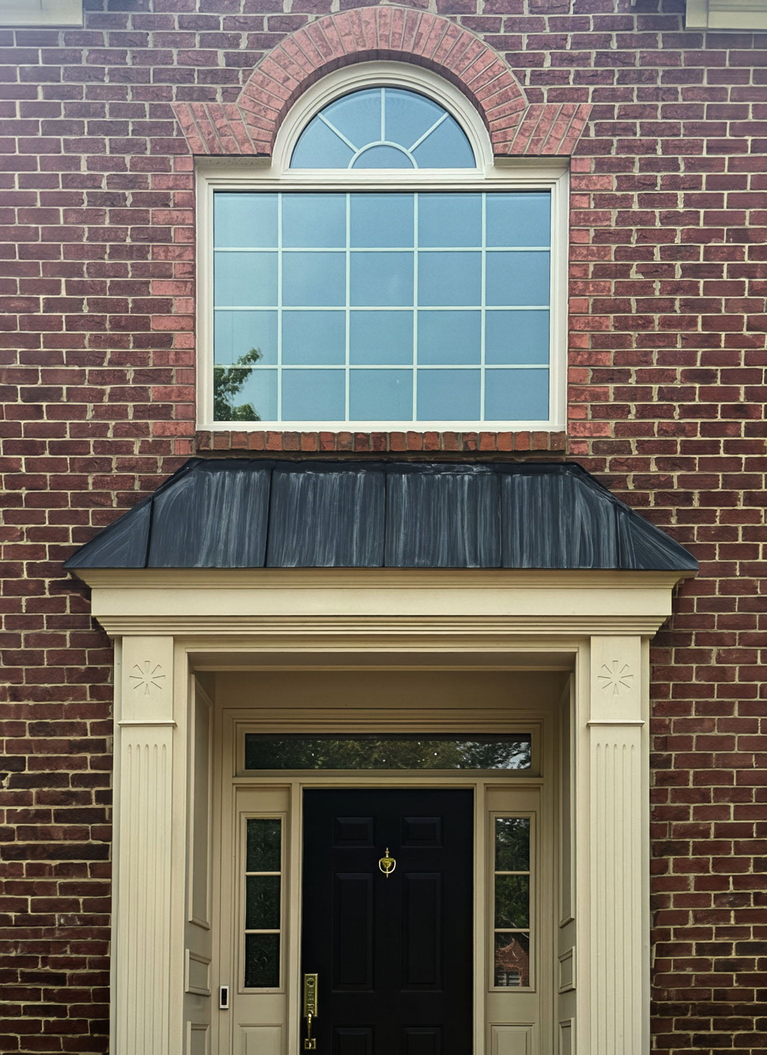 Arched replacement window above a front entry door on a brick house with cream trim and black door.
