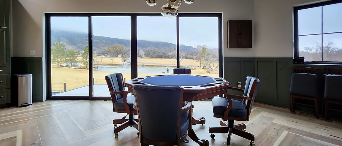 A modern gaming room featuring a poker table with blue felt and black multi slide patio door, overlooking a scenic view.