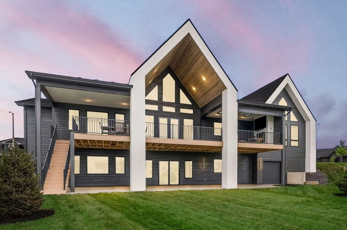 Rear view of modern home featuring covered deck, balconies, and large gabled windows.