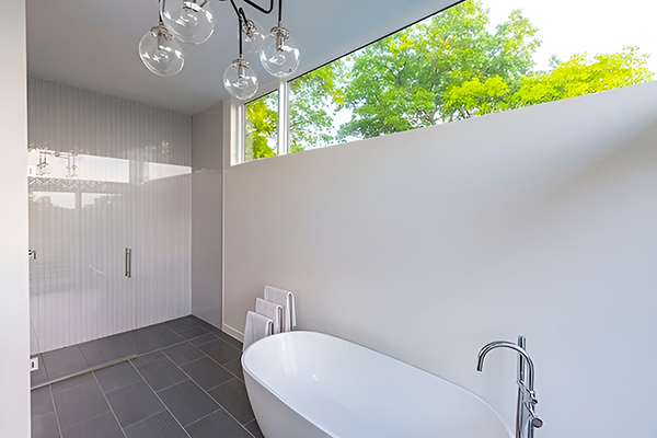 White modern bathroom with glass shower frame, white tub, and high fixed windows