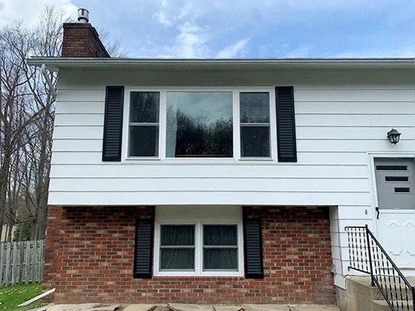 After picture window view of a home exterior with white siding and brick, featuring black shutters.