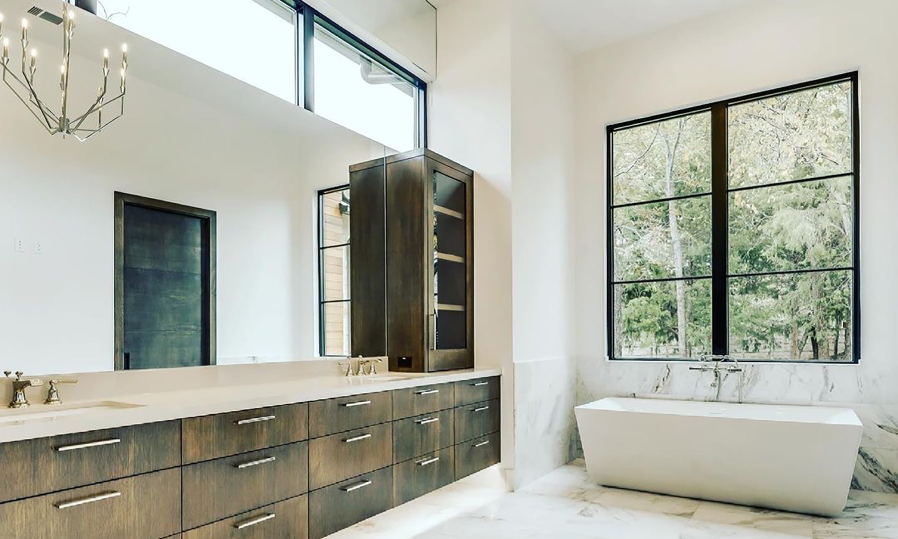 A contemporary bathroom with black picture windows over the white bathtub and wood vanity.