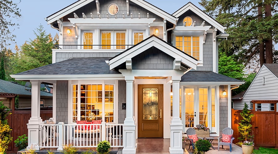 A home at dusk with all lights on inside that is also shining through the entry door with decorative glass.