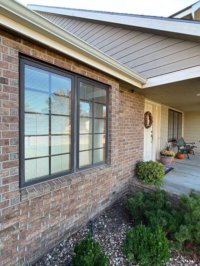 Before image of a brick house exterior featuring casement windows and landscaped shrubs.