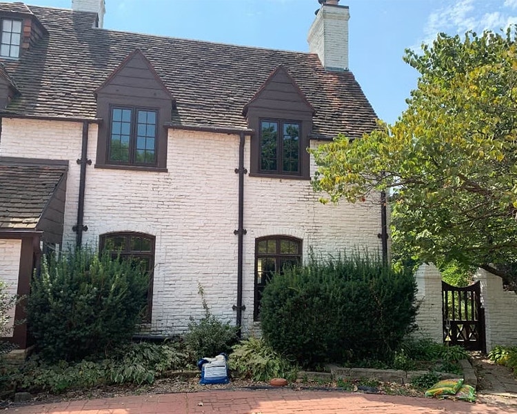 A large white historical home with brown wood windows and a circular brick courtyard.