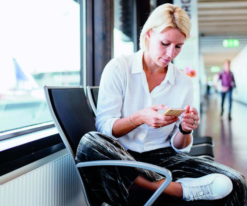 a woman sitting in an airport looking at her phone monitoring her home via the insynctive app