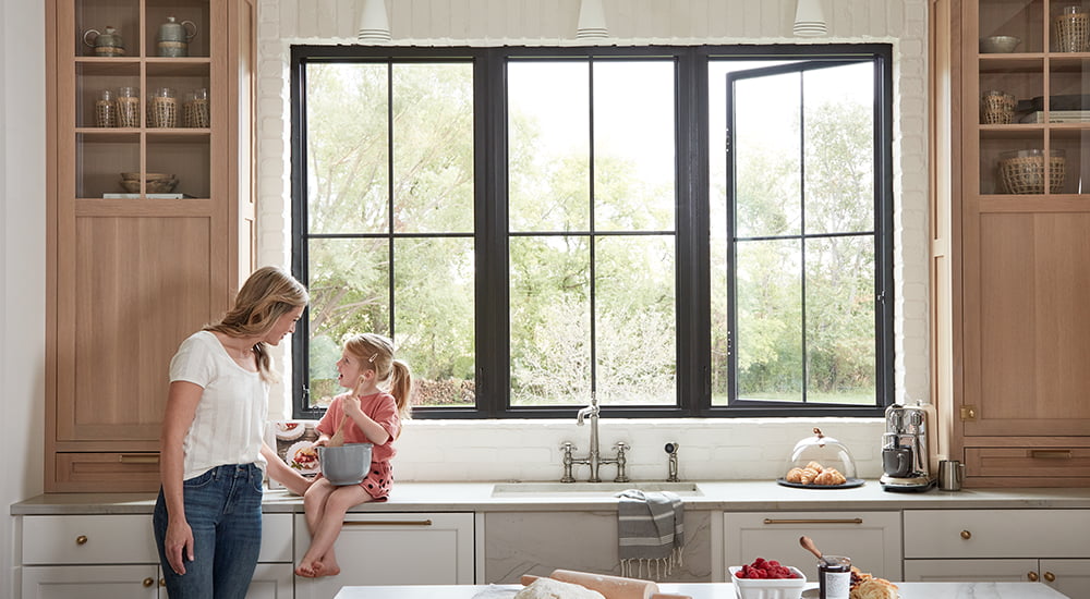 a mother and daughter enjoy baking together with three black casement windows in the background