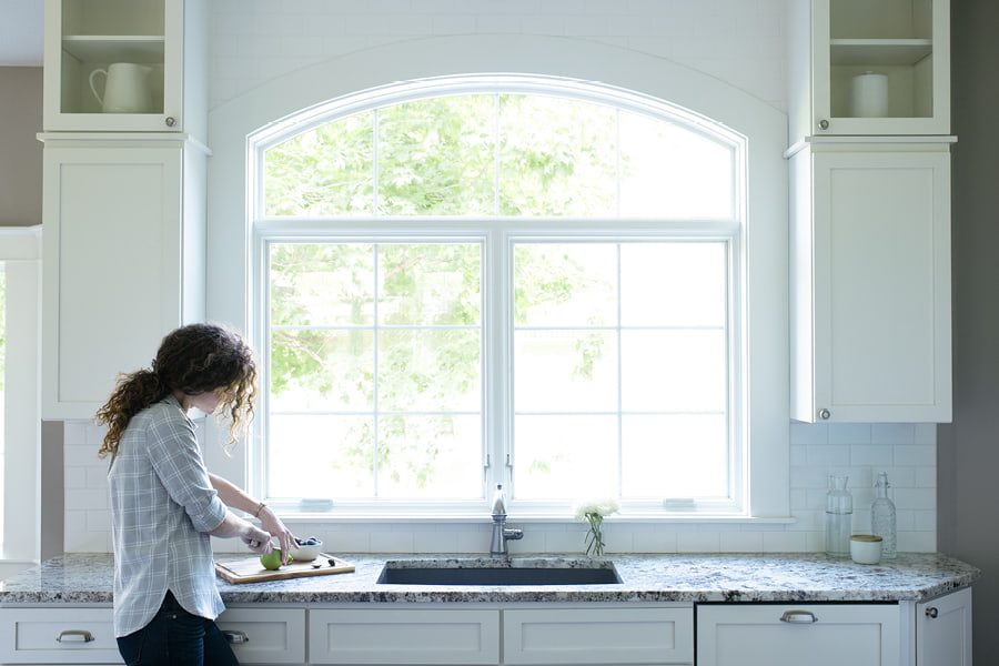 White arched window over kitchen sink with a girl cutting a green apple
