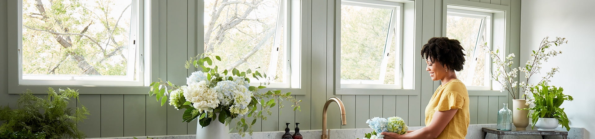 woman in a yellow shirt standing in kitchen by four awning windows