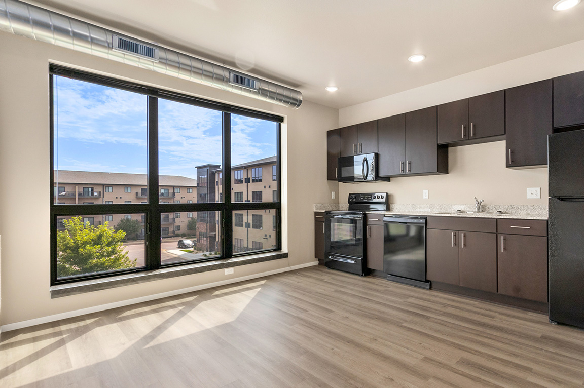 Spacious apartment with large windows, modern kitchen, and view of other apartment windows outside.