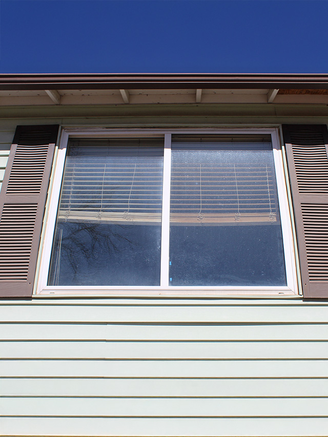 A white 250 series window with brown shutters on a home exterior in Aurora, CO.