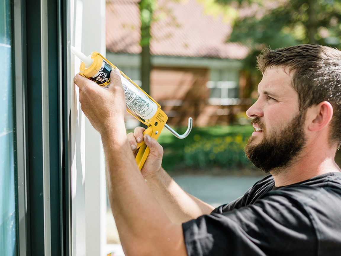 A man applying caulking during the installation of bow windows, ensuring a tight seal.