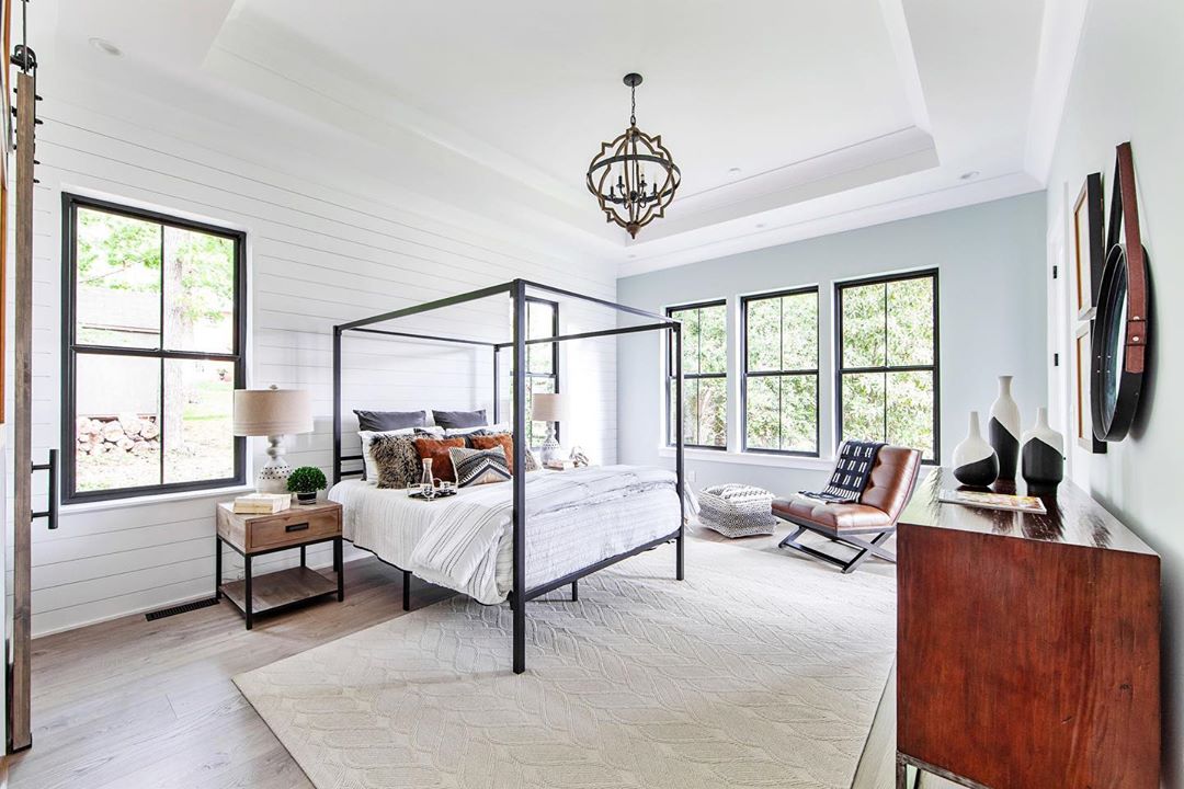 contemporary bedroom with four poster bed, chandelier, and black double-hung windows