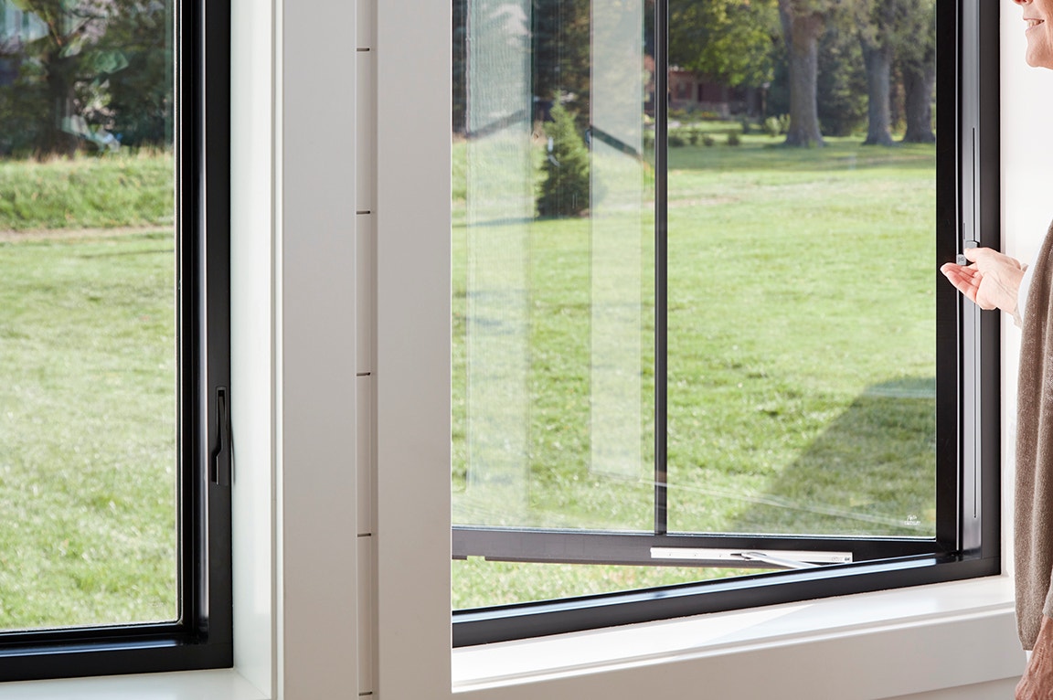 A modern window glass with a black frame, partially open, showcasing a view of green grass outside.