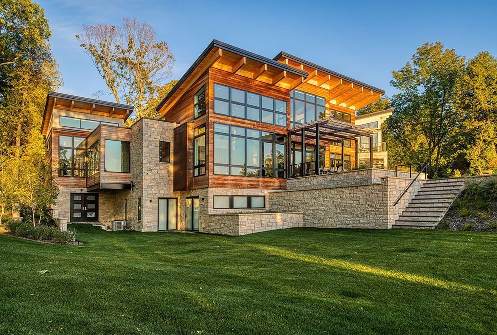 A modern home has wood siding, stonework and walls of black windows and sliding patio doors.