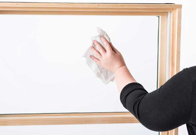 Hand holding a rag and wiping the glass panel of a double-hung window.