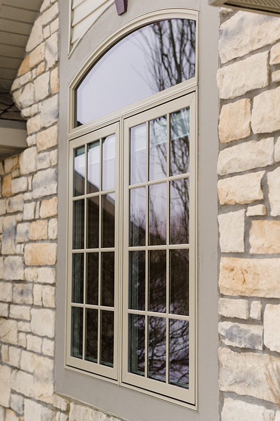 A tan window with an arched design set in a stone exterior.