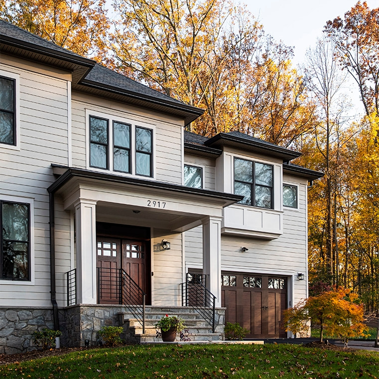 Modern house with brown windows surrounded by autumn foliage, showcasing a welcoming entrance.