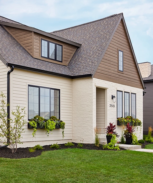 A home exterior that has window boxes filled with several varieties of greenery as well as front potted plants aside the entrance.