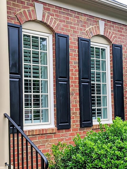 Two tall casement windows on a brick home exterior with black shutters