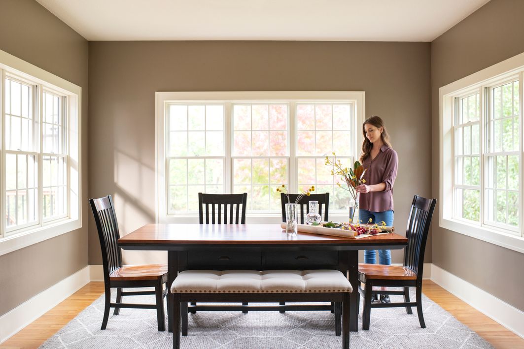 Woman arranging flowers in dining room area with white wood windows