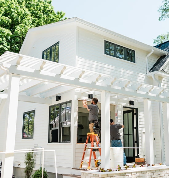 two contractors adding new windows to a farmhouse-style home