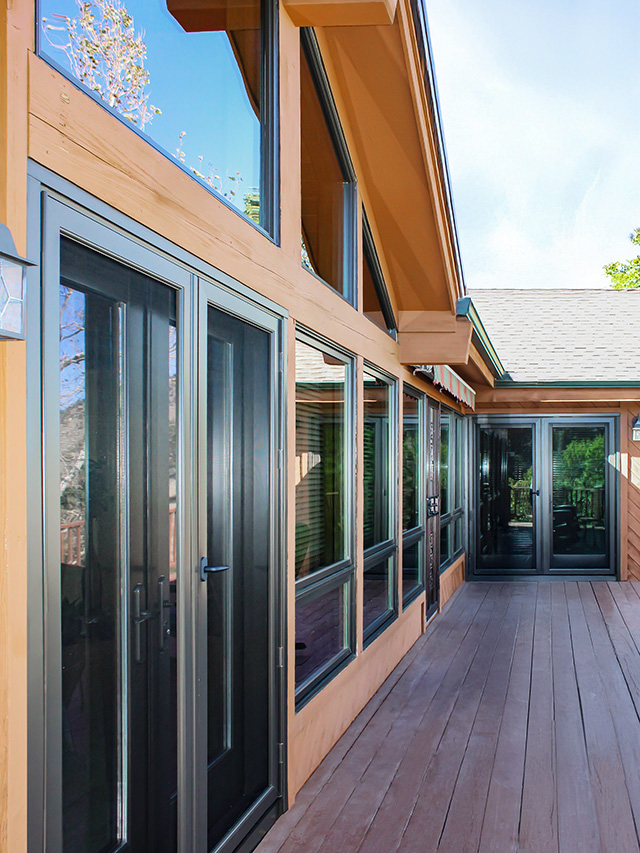 Modern wooden deck with large glass doors and windows on a contemporary home exterior