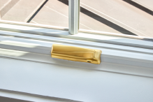 A white Pella casement window with the fold-away crank in a brushed gold finish.